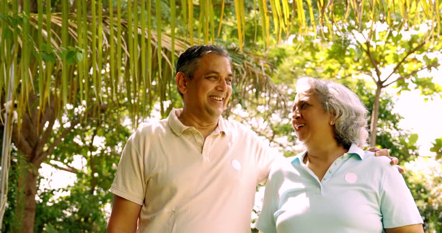 Indian Asian mid age couple in their fifties walking in the park, smiling and pointing, enjoying a pleasant conversation on a sunny day outdoors