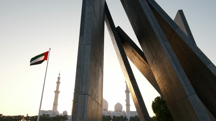 peaceful view from Wahat Al Karama Park at sunset, with golden light casting warm glow over serene landscape. iconic Sheikh Zayed Mosque stands beautifully in background, creating breathtaking scene.