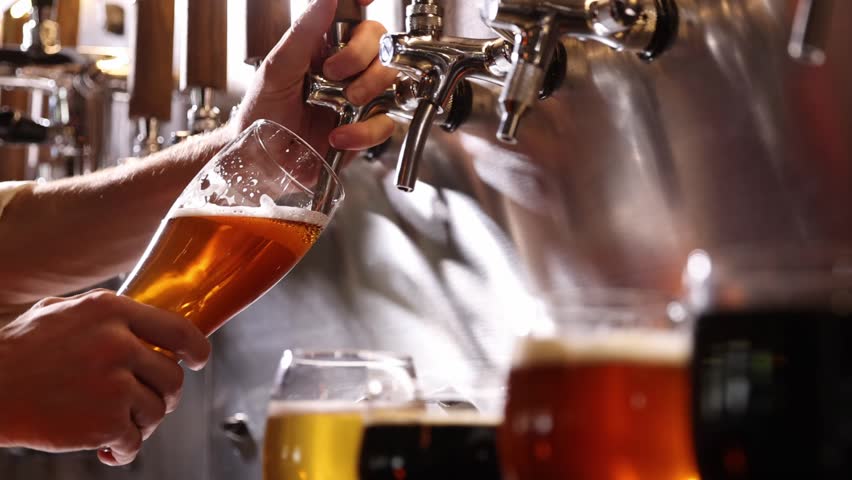 Bartender pouring beer into glasses at pub in neon light. Close-up view of barman's hand filling glass with light beer. Beer craft. Bar table. Oktoberfest, party, drinks, taste and alcohol concept.