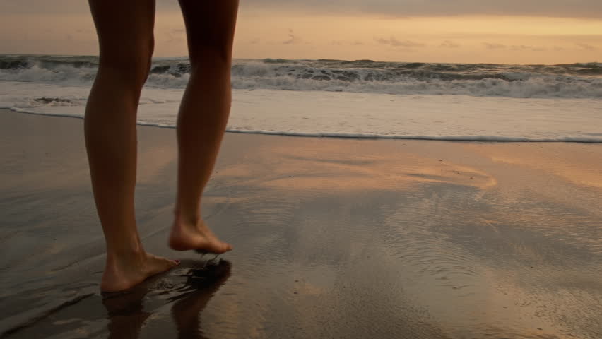 Woman or female feet barefoot on ocean beach. Tourist walking on the beach or coast by sea, enjoying the sunrise or sunset. Close up of legs and feet in the sea water. Travel, summer outdoors concept