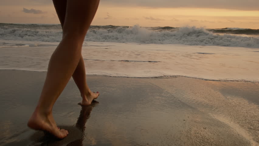 Woman or female feet barefoot on ocean beach. Tourist walking on the beach or coast by sea, enjoying the sunrise or sunset. Close up of legs and feet in the sea water. Travel, summer outdoors concept