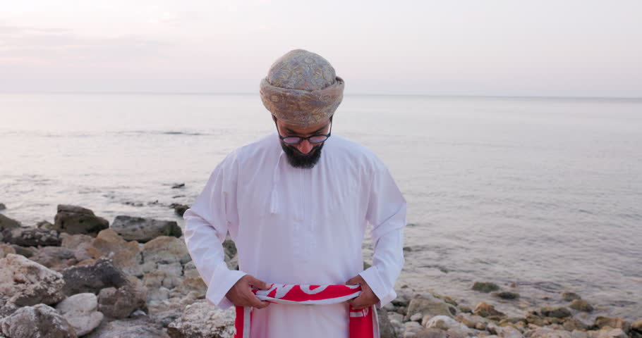 Front view of an Omani man with Oman scarf flag , wearing omani traditional dishdasha and Musaar