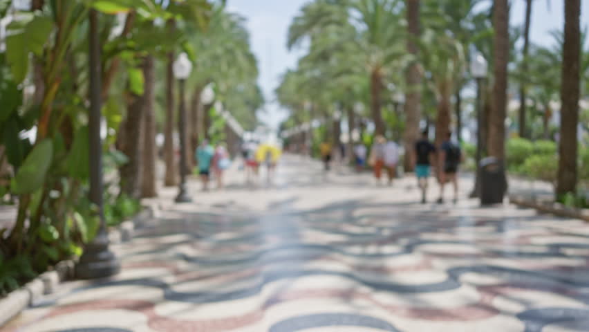 Defocused view of people walking along the palm tree-lined rambla in alicante, spain, showcasing a vibrant outdoor atmosphere