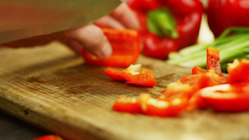 Slow motion video of slicing a red pepper with a knife on a cutting board. High quality 4k footage