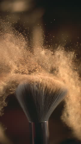Makeup brush and golden face powder shake at 1000 fps. Elegant luxury make up cosmetic macro abstract background in super slow motion. Beauty make-up glitter flying. High speed close up vertical video