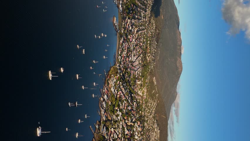 Boats moored along shores of Derwent River at Hobart city, Tasmania in Australia. Aerial drone backward and Vertical Format