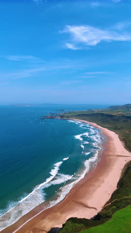 Narrow sandy beach at the coast of the Atlantic Ocean. Footage above the rocky shore of Ireland on sunny day. Vertical video.