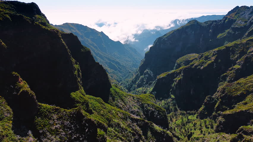 Steep rocks covered with mosses. Drone flies over the mountains with white clouds covering the tops.