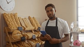 Young man in a bakery holding a tablet surrounded by fresh bread and pastries with prices displayed on shelves - Powered by Shutterstock - Get 15% off with code: PIKWIZARD15