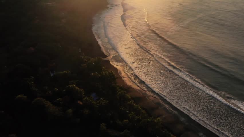 Aerial footage of a stunning beach sunrise over the Pacific Ocean It begins with waves from above shifting to the coastline and horizon where the sun rises over lush mountains blending sea sand nature