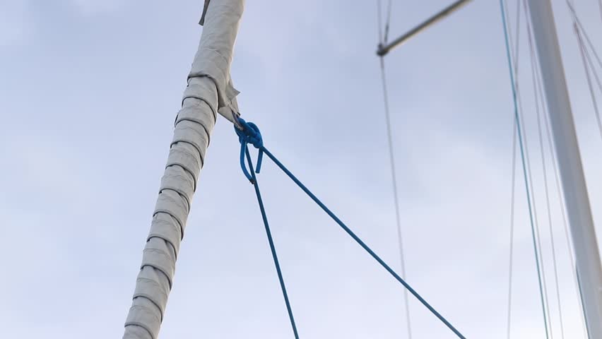 Furled sail against the sky. Furling sail on a sailing yacht. Close-up of a small yacht's sail. Boats with masts. White sail furled on a sailboat's stay