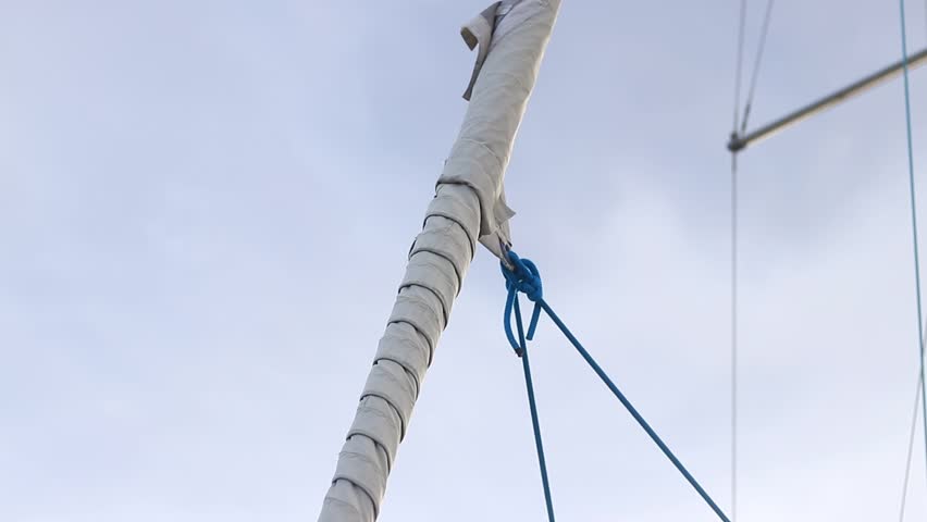 Furled sail against the sky. Furling sail on a sailing yacht. Close-up of a small yacht's sail. Boats with masts. White sail furled on a sailboat's stay