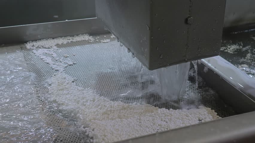 Close up: process of filtration, separation the plastic material: fast water flow with recycled plastic granules, pellets. Plastic pelletizer recycling machine. Waste reduction and sustainable concept
