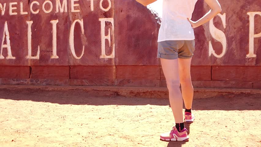 SLOW MOTION: tourist woman at Alice Springs Welcome Sign in Central Australia, Northern Territory. Tourism in Outback Red Center desert. Travel discovery road in Australian trip in dry summer season