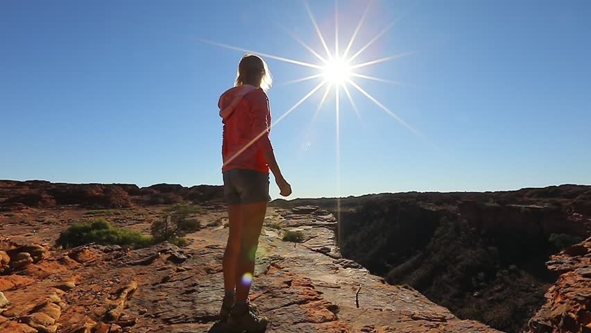 Young hiking girl jumping at Kings Canyon. Enjoying in Red Center Outback. Jumper among sandstone formations in Watarrka National Park. King Canyon Rim Walk at sunset. Northern Territory, Australia.
