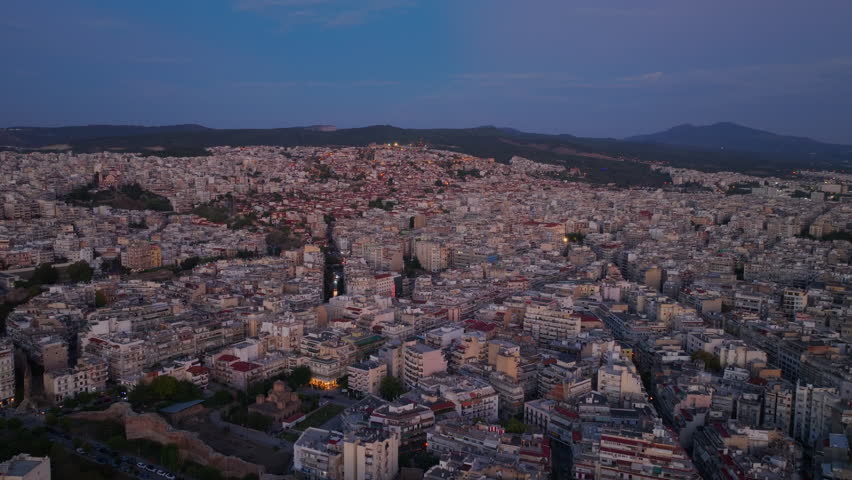 Aerial view of Thessaloniki, slowly illuminates as the blue hour descends upon the Greek city. Cars drive down a main road towards the Ministry of Macedonia and Thrace