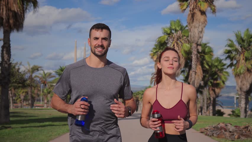 Young couple running outdoors in a tropical setting with palm trees in the background. Fit man and woman jogging together, enjoying an active lifestyle, fitness, and exercise in a scenic, sunny