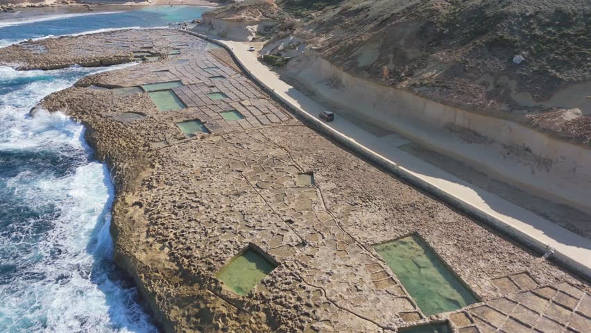 Aerial follows car drive at Salt panes Gozo Malta road, coastline landscape, natural environment, travel destination