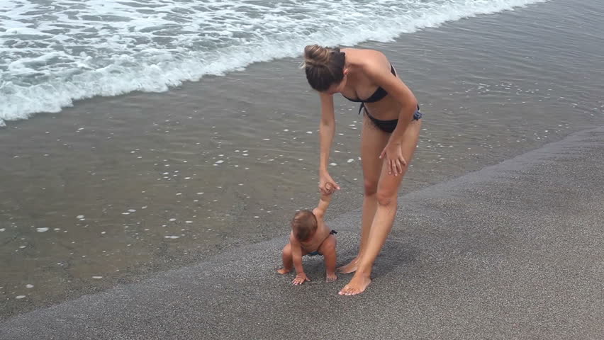 Mother holding daughter by hand and walking at coastline