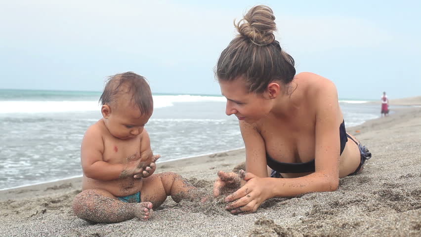 Beautiful mother and girl lying at beach playing with sand