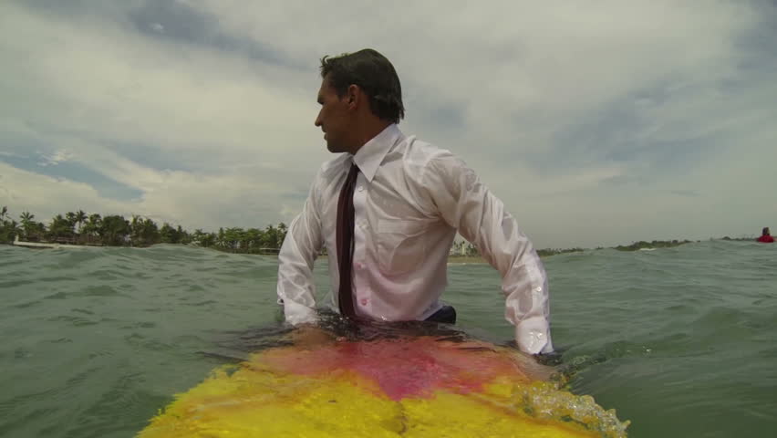Happy businessman sitting on surfboard in ocean