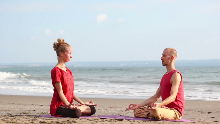 Couple sitting in pose lotus and practicing yoga on beach