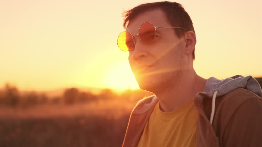 A man enjoys the warm glow of sunset while standing in a serene field during golden hour, reflecting on the days events