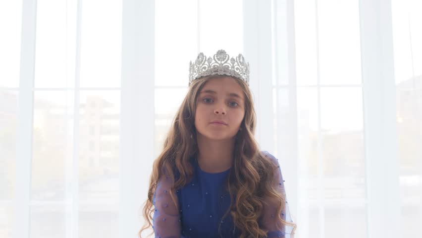 Portrait of a cute little princess with a crown on her head. The girl winks and smiles at the camera.