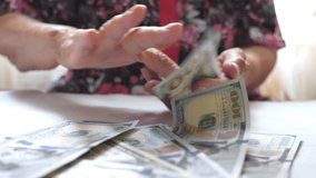 Grandmother holding bundle of money in hands and throwing one hundred dollar bills on the table. Arms of old woman scattering foreign currency on the desk in front to camera. Close up Slow motion - Powered by Shutterstock - Get 15% off with code: PIKWIZARD15
