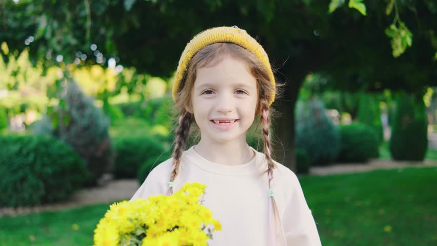 A little girl holding beautiful yellow flowers standing in the autumn park, enjoying a carefree day outdoors