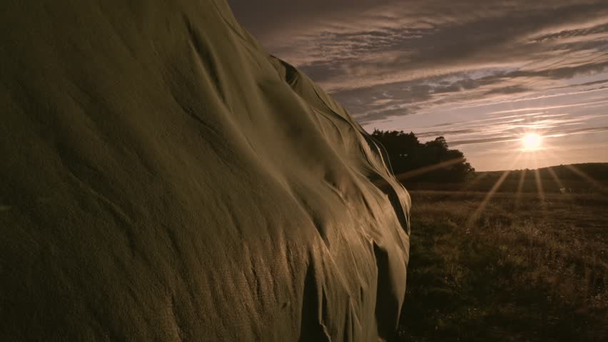 Hay bales covered with a tarp under dark skies in rural Brandenburg, Germany, tarp swaying in wind