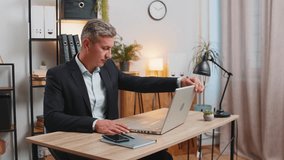Young gray-haired businessman freelancer in formal suit opens laptop start working sends messages, watching movies, makes online purchases. Caucasian guy using netbook in modern home office workspace. - Powered by Shutterstock - Get 15% off with code: PIKWIZARD15