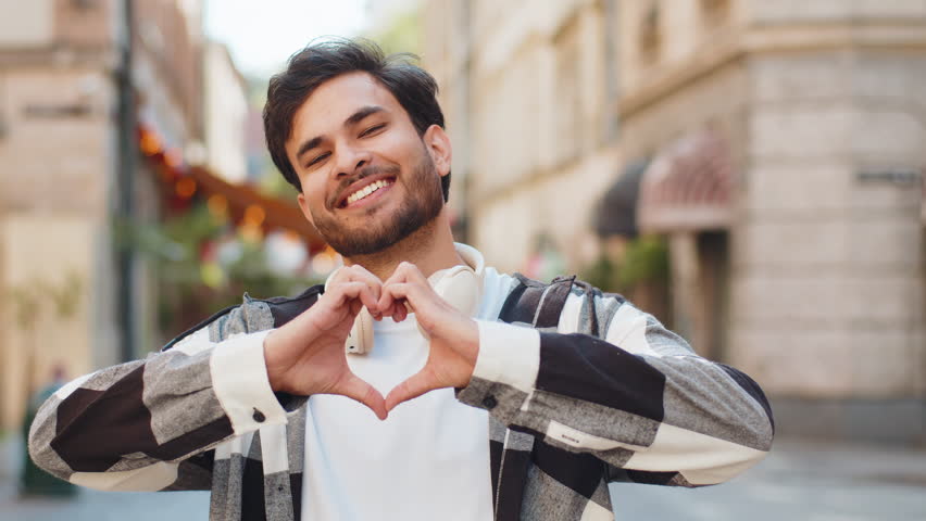 I love you. Indian man makes symbol of love, showing heart sign to camera, express romantic feelings, express sincere positive feelings. Charity, gratitude, donation. Outdoors in urban city street.