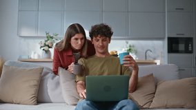 Home couple looking laptop at modern living room. Relaxed man sitting sofa sharing coffee with woman shopping online on computer. Happy young partners discussing purchase in e-commerce store in flat  - Powered by Shutterstock - Get 15% off with code: PIKWIZARD15