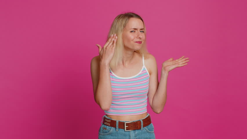 I cant hear you. What. Caucasian woman trying hear you looking confused and frowning keeping arm near ear for louder voice asking to repeat, to hear information deafness. Young girl on pink background