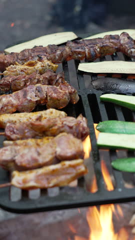 Grilling zucchini slices, corn on the cob, sausages, and skewered meat over an open flame at a campfire. Mixed variety of food grilling on a barbeque in an outdoor forest setting