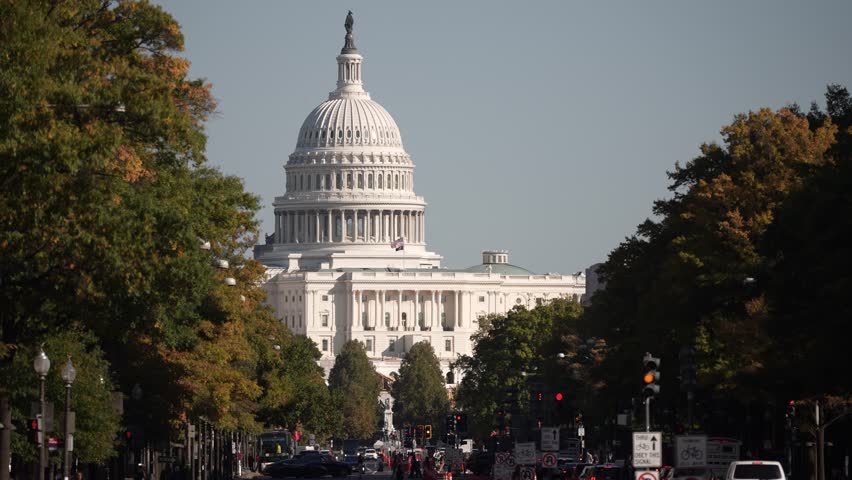 A view of the US Capitol building in Washington DC with fall foliage in the foreground and traffic lights and street signs in the foreground.