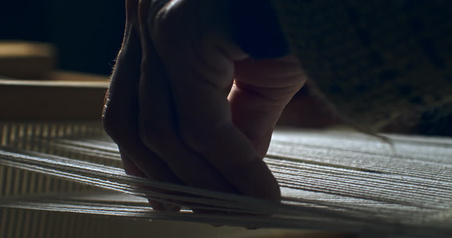Super slow motion macro of artisan touching threads with flying dust or talc powder particles splashing around, while working with woven weaving machine to craft cloth piece in workshop at 1000 fps. 