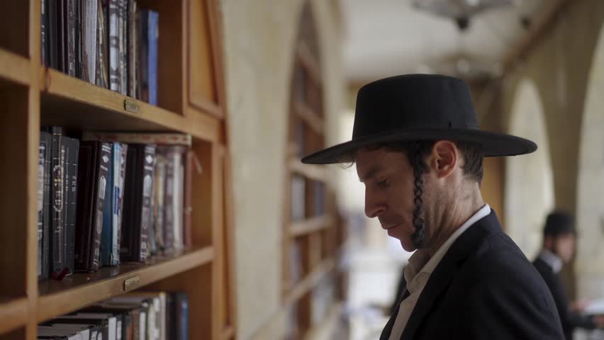 Male Orthodox Jew Getting Talmud Book From Bookshelf At Synagogue In Jerusalem, Israel. side view, slow motion