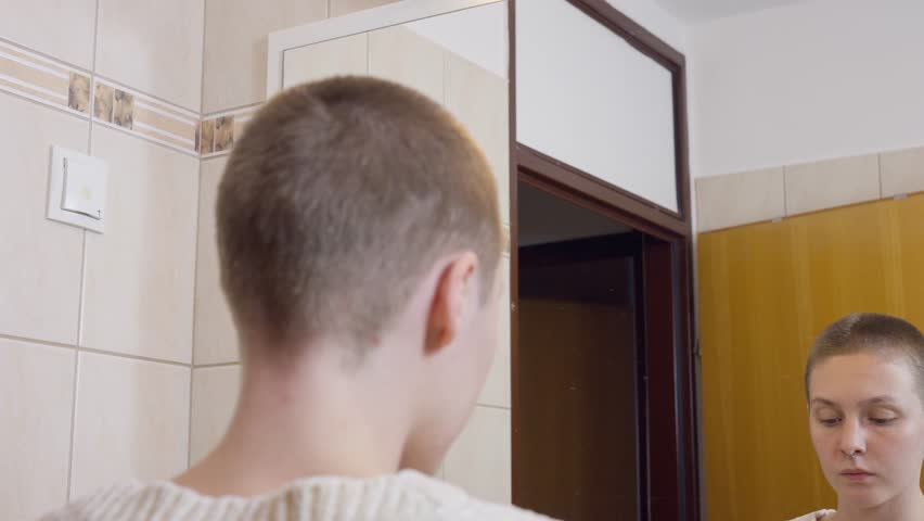 A woman confidently shaves her head in front of a bathroom mirror, embracing a bold new look, self-expression, courage, boldness, close-up, close up, new year resolution, new beginning bathroom bright