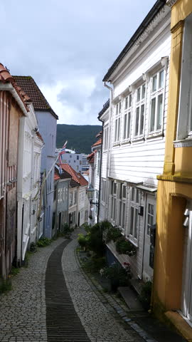 Vertical video. Walking downhill narrow cobbled street in Nostet area of Bergenhus district in Bergen, Norway. Personal point of view, POV, handheld camera shot.