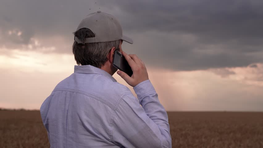 Farmer man in wheat field talking on mobile phone. Businessman talking on smartphone in wheat field in summer. Agricultural business. Rain cloud over wheat field. Agronomist working on plantation, sky