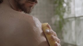 Close-up of young Caucasian man cleaning herself with soapy sponge from shoulder to neck relaxing in shower. Adult long haired male doing daily hygiene and body care alone in bathroom  - Powered by Shutterstock - Get 15% off with code: PIKWIZARD15