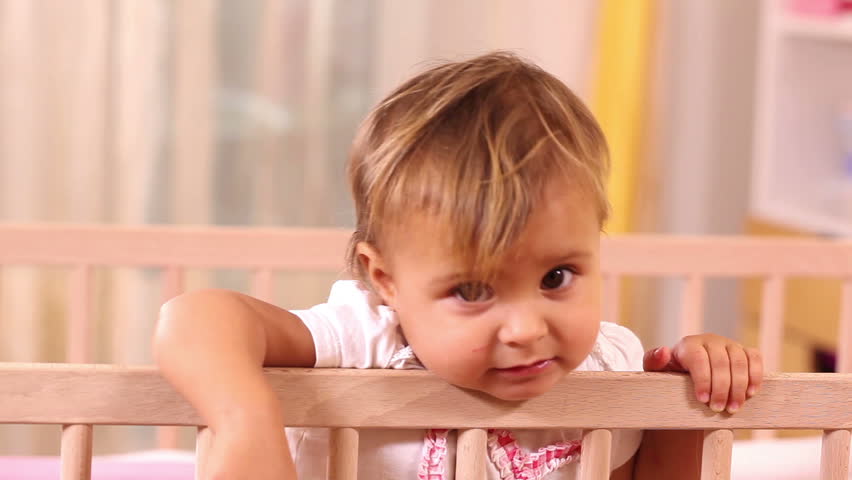 Adorable small girl standing in her bed and looking at camera