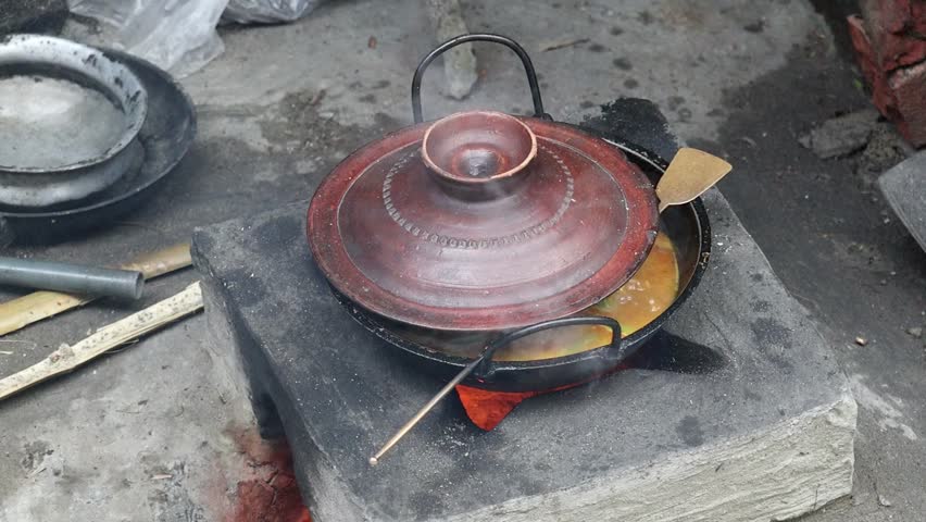 Village cooking on a traditional clay stove in Bangladesh. The curry, covered with a lid to simmer, steams. These stoves made of clay and fueled with wood, commonly used by residents in rural areas.