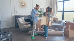 Young diverse family of African American woman and Caucasian man have moved into apartment in new city and are discussing where to hang painting in living room with fireplace and scattered boxes. - Powered by Shutterstock - Get 15% off with code: PIKWIZARD15