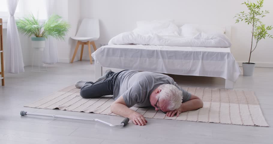 Young male nurse trying to provide first aid emergency helping senior patient lying on the floor with walking stick at home suffering with pain. Nurse support concept. 4k video. Slow motion video.