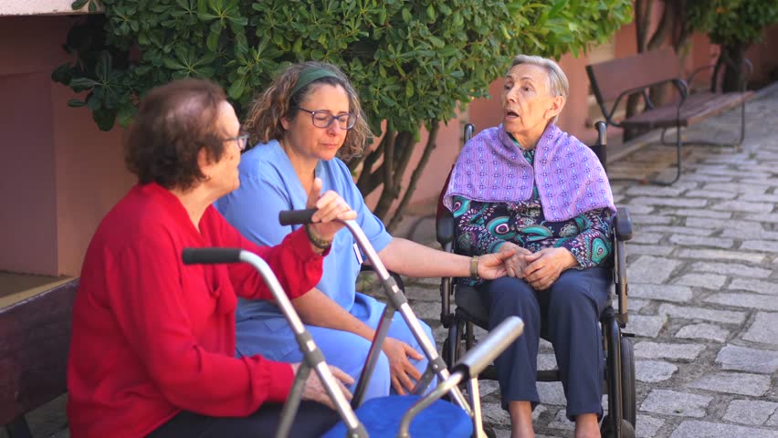 Female nurse and senior woman talking and relaxing in the garden of nursing home
