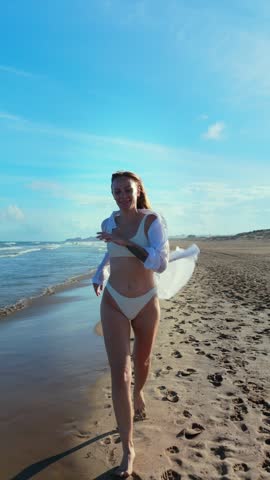 Drone Video Young Woman in White Swimsuit Run Along Beach, Embracing Freedom and Joy Under Sunny Sky. Vertical Video