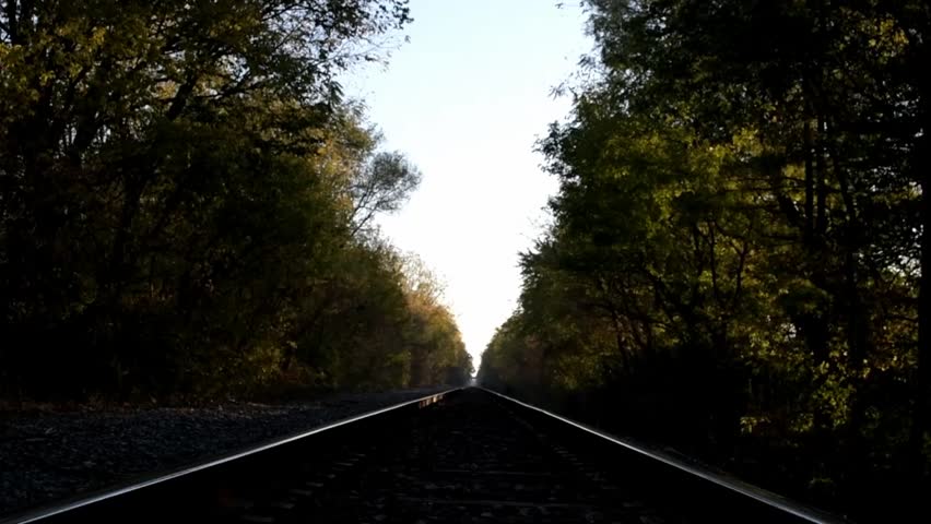 Man alone walking away from the camera down a railroad tracks in the darkness of early morning.